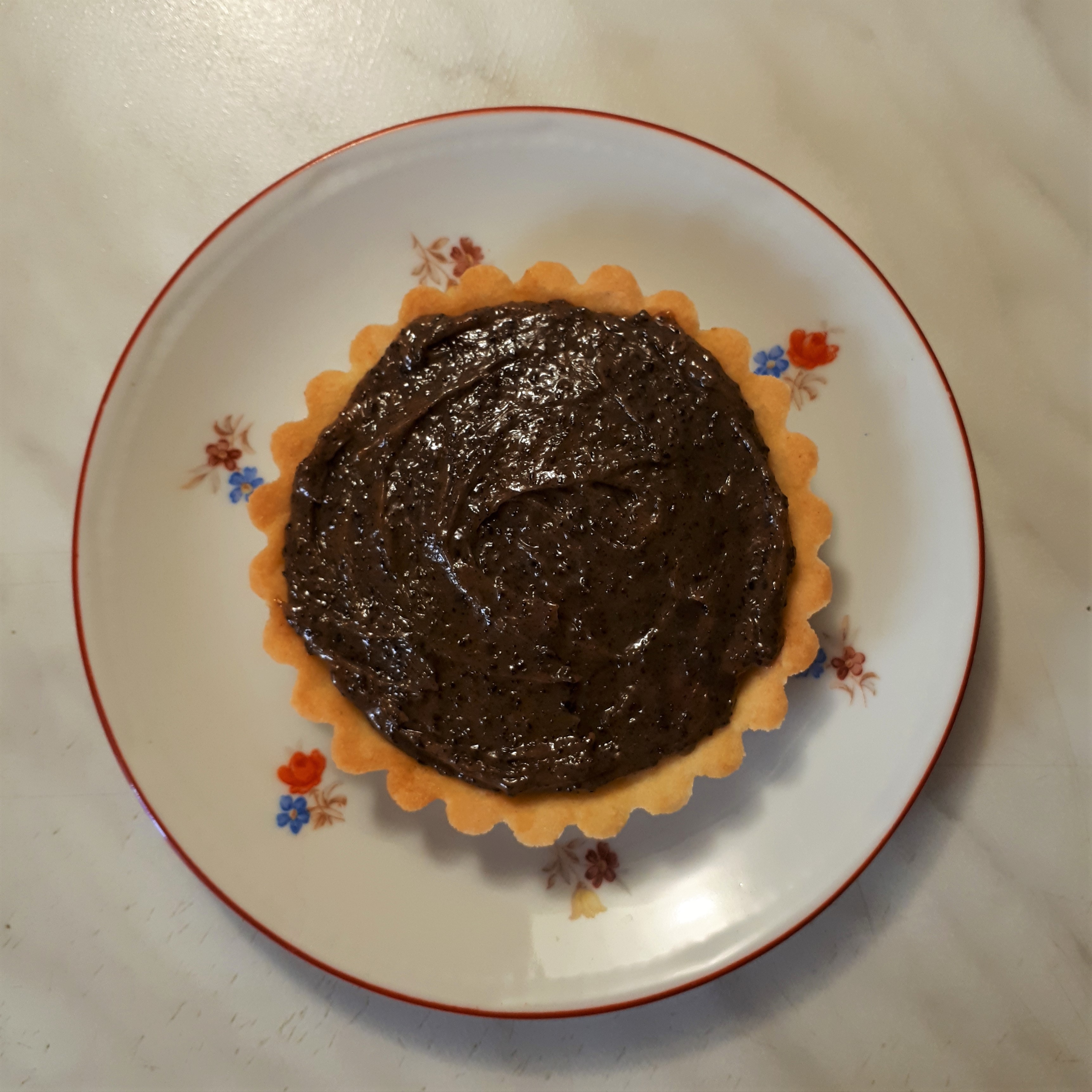 Tartaletka zo svetlého krehkého cesta s kávovou ganache biely tanierik s červeným okrajom a drobnými kvietkami