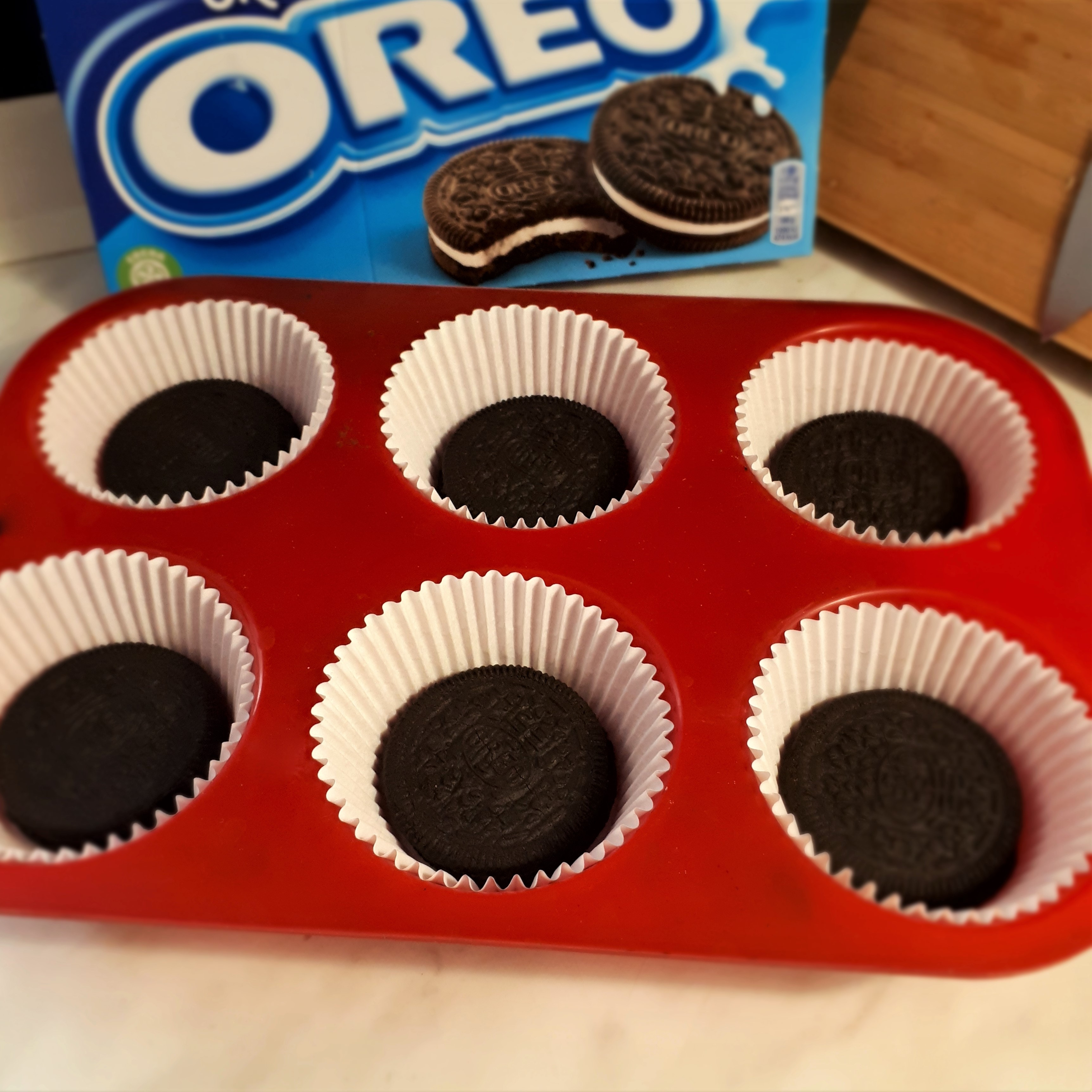 Červená forma na muffiny 6 bielych papierových košíčkov na dne každého Oreo sušienka v pozadí krabica Oreo sušienok