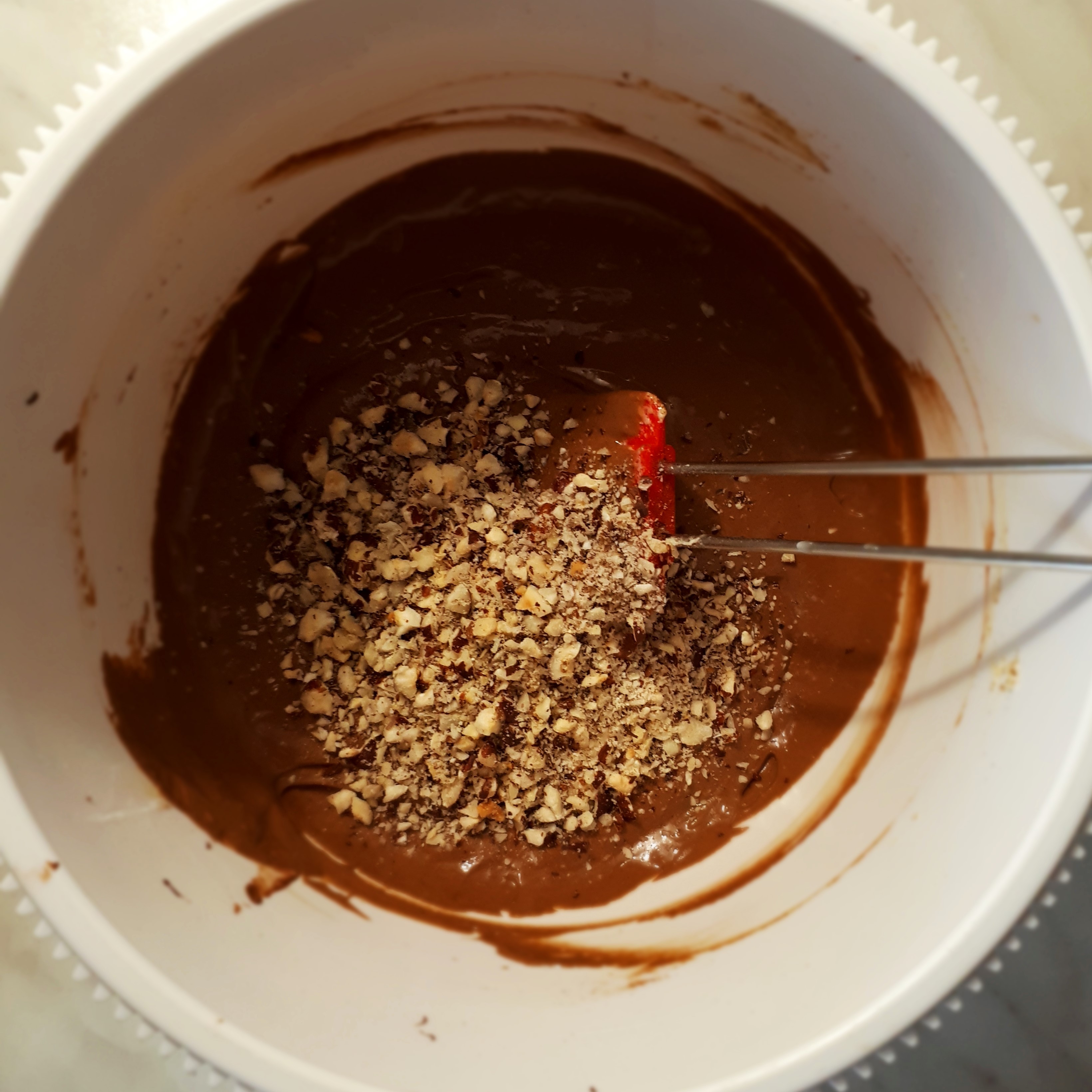 Biela misa s čokoládovým cestom na brownies a rozmixovanými lieskovými orechmi červená cukrárska stierka na mramorovom povrchu