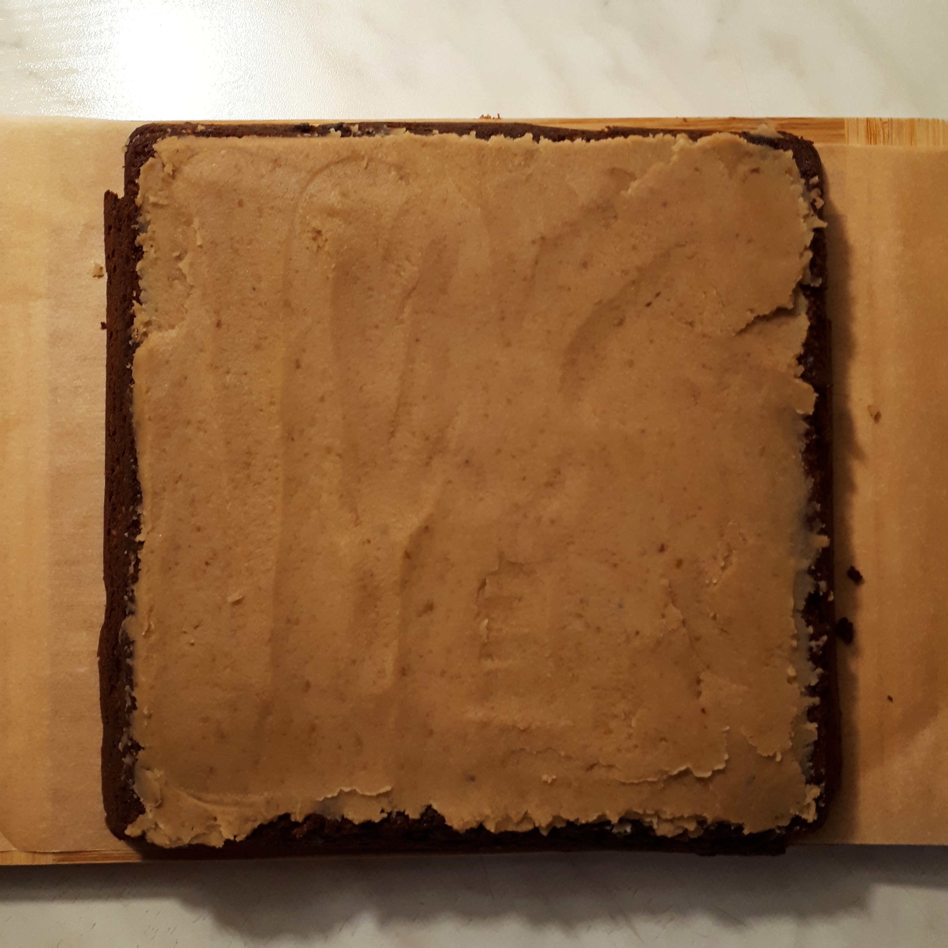 Upečené brownies na drevenej doske s papierom na pečenie potreté gaštanovým pyré na mramorovom povrchu