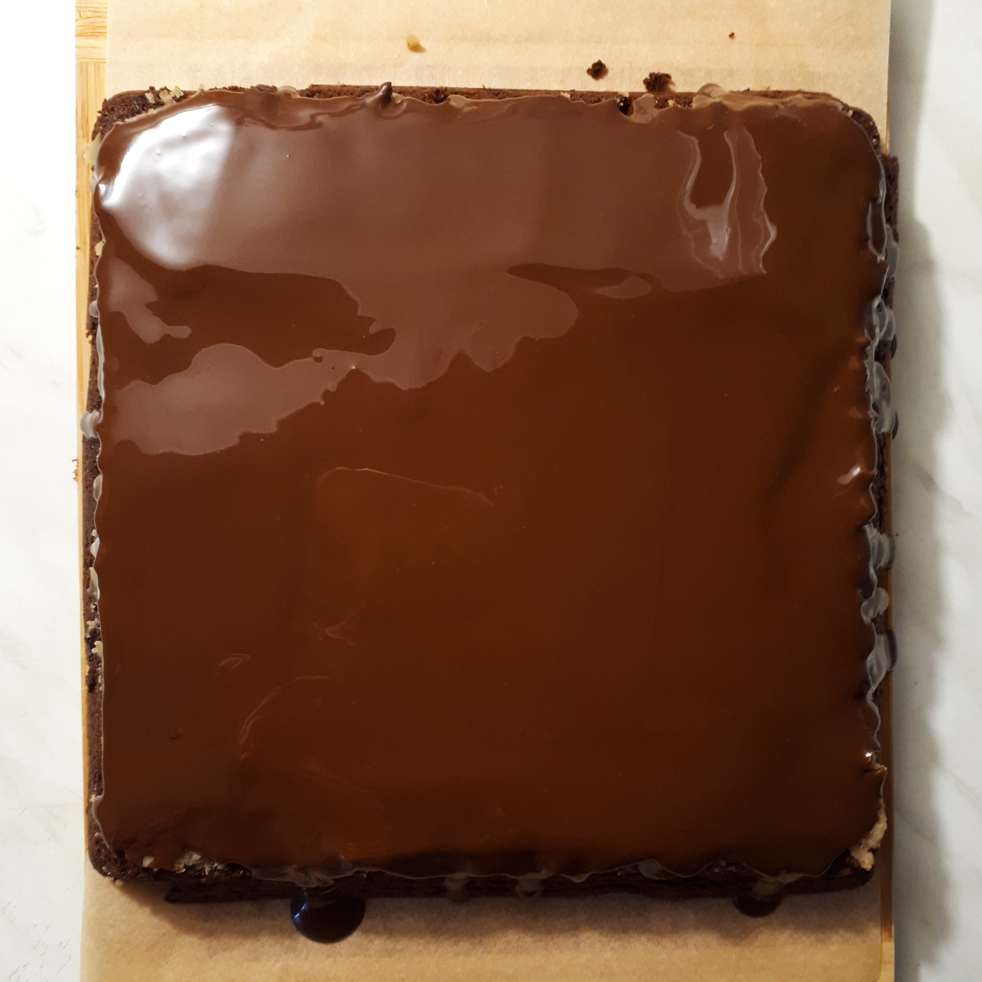 Upečené brownies na drevenej doske s papierom na pečenie potreté gaštanovým pyré a preliate čokoládou na mramorovom povrchu