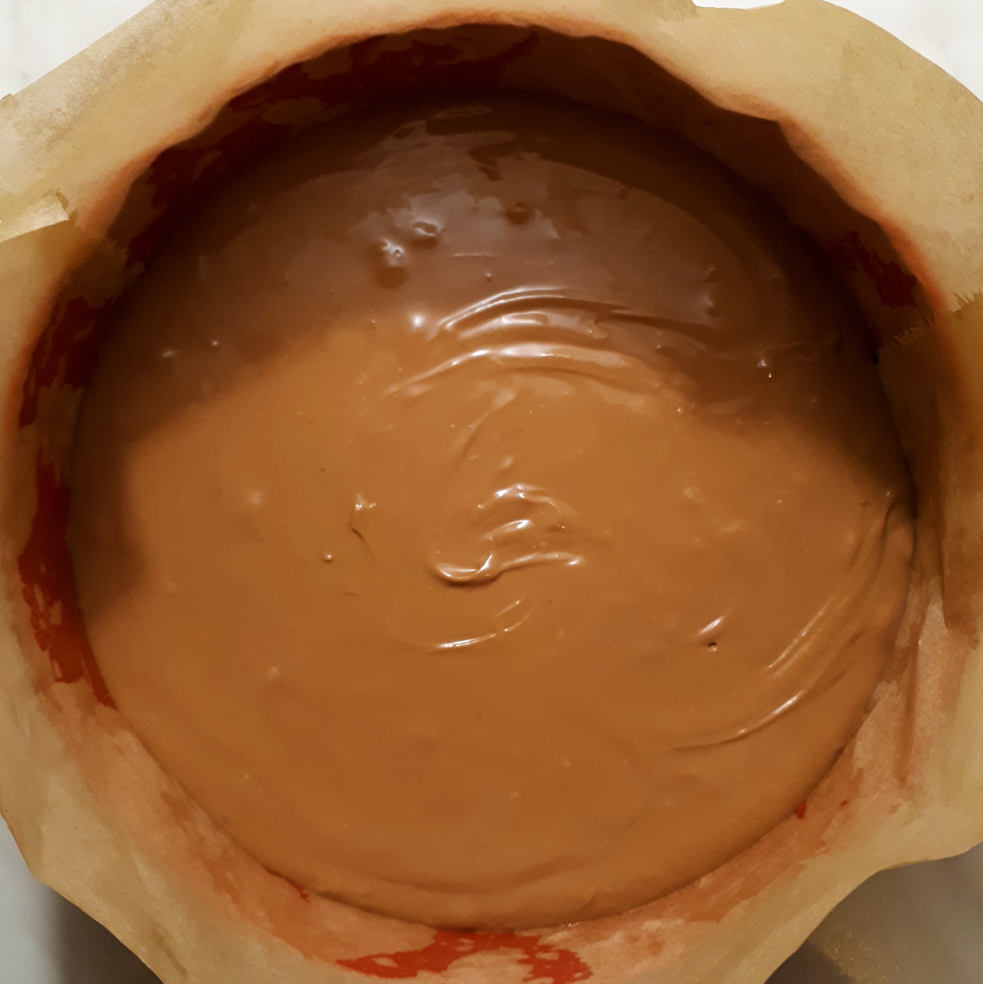 Červená okrúhla tortová forma vystlaná papierom na pečenie s cheesecake krémom s čokoládou a chilli