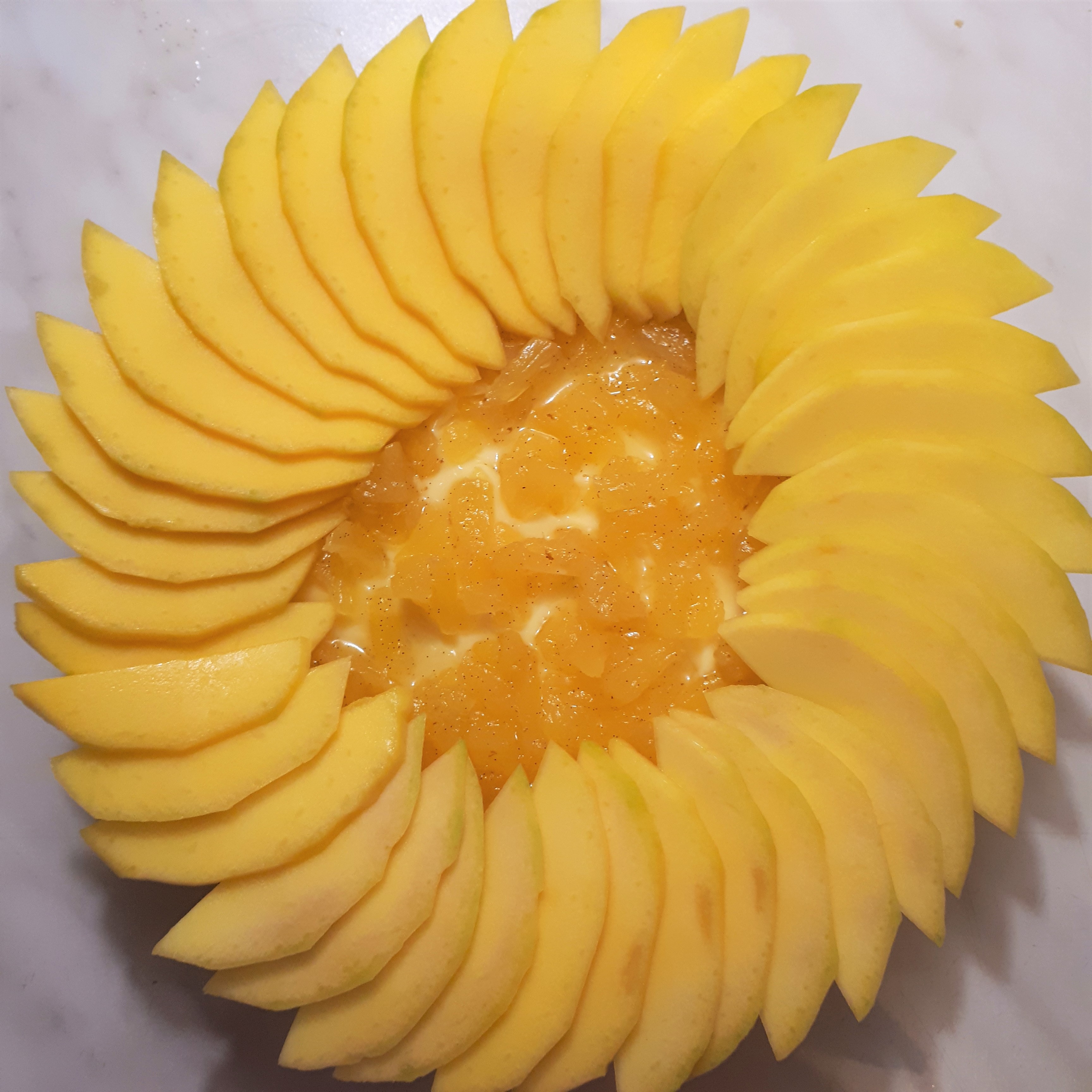 Upečený korpus na tart naplnený vanilkovým krémom a vanilkovým ananásom nakrájaným na kúsky dokola obložený plátkami manga na mramorovom povrchu