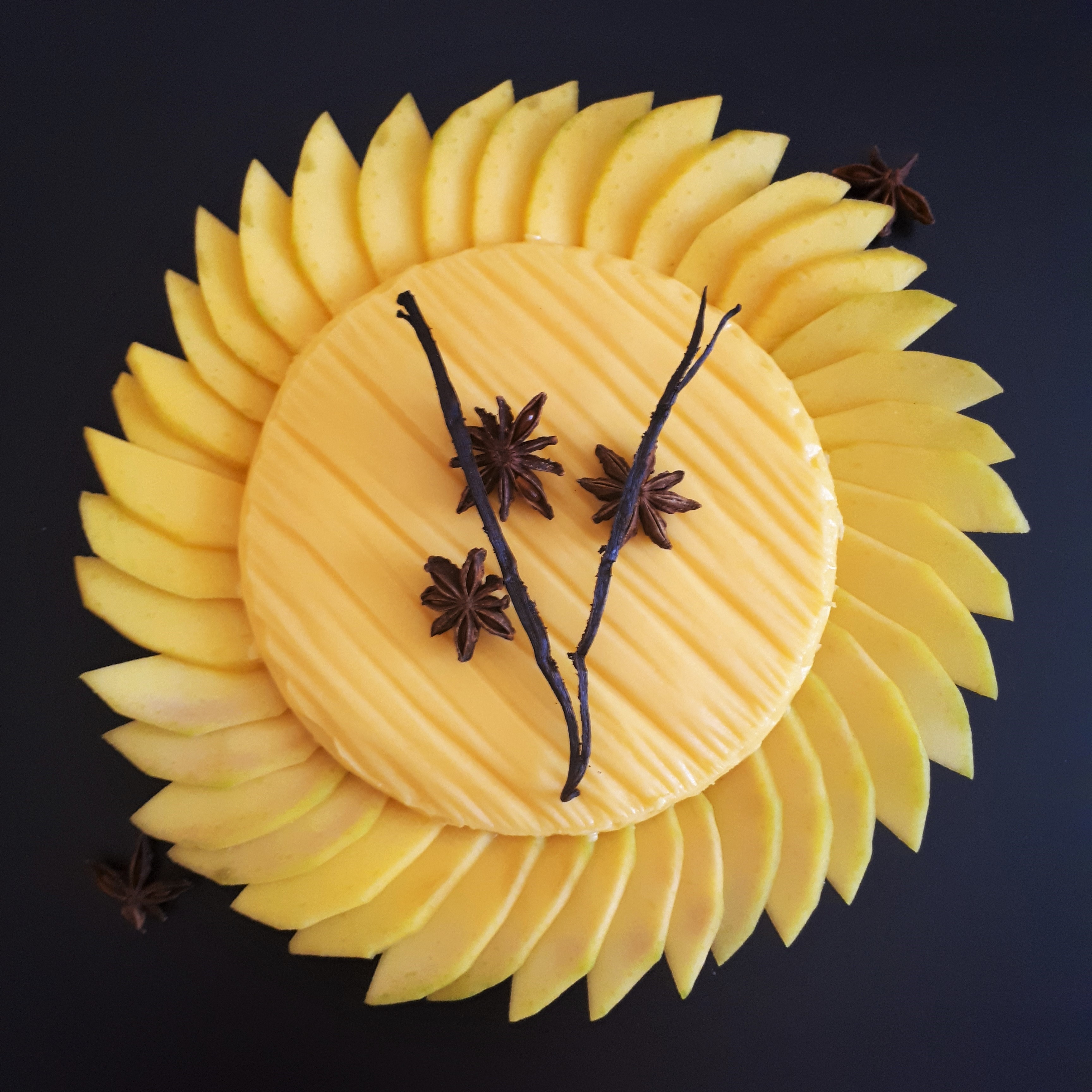 Upečený korpus na tart naplnený vanilkovým krémom a vanilkovým ananásom nakrájaným na kúsky dokola obložený plátkami manga dozdobený vanilkovým strukom a hviezdičkami badiánu na mramorovom povrchu