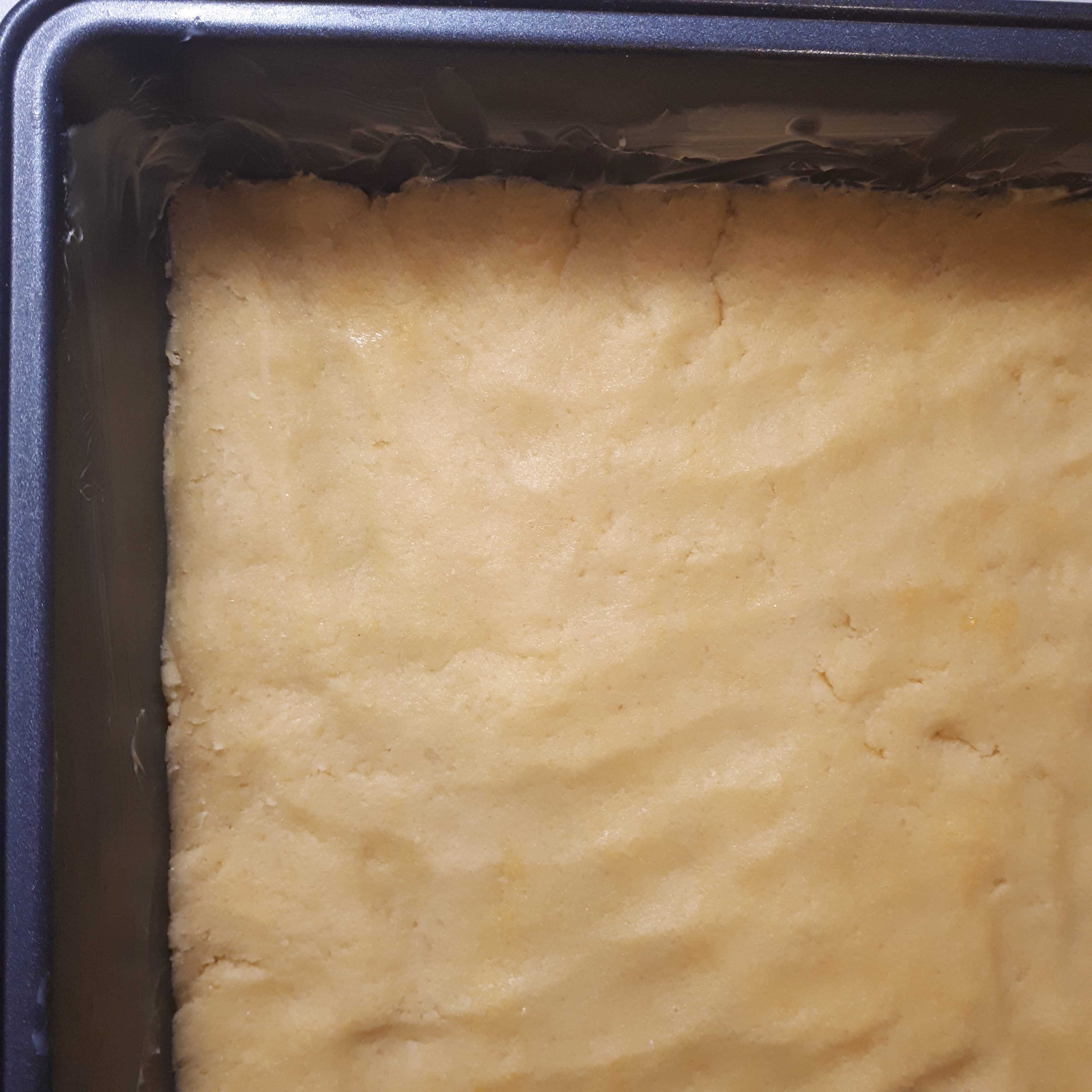 Maslové cesto vtlačené na dno čiernej antikorovej formy na pečenie vymazanej maslom