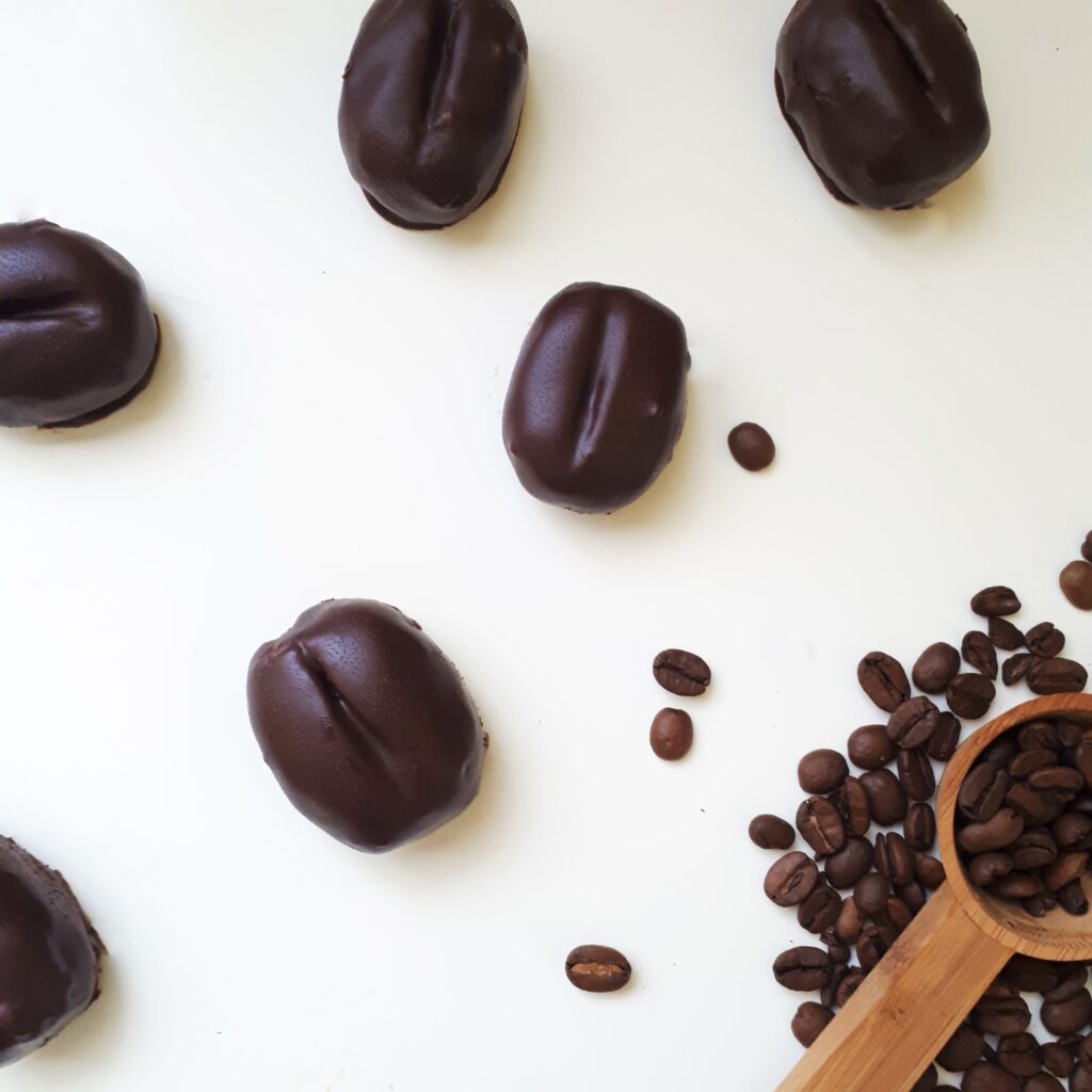 Šesť kávových zŕn b čokoláde na bielom povrchu odmerka na kávu rozsypané zrnká kávy