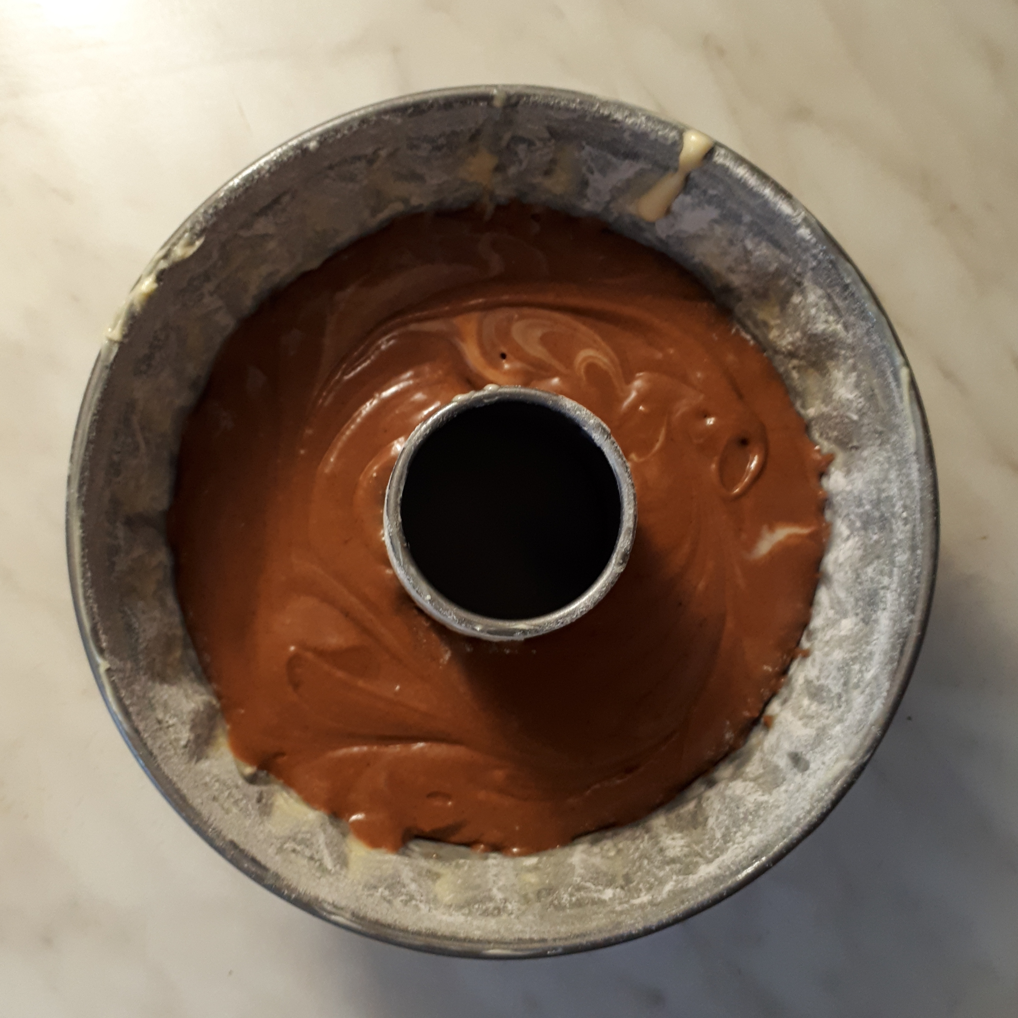 Bábovková forma vysypaná múkou s cestom svetlým a čokoládovým na mramorovom povrchu