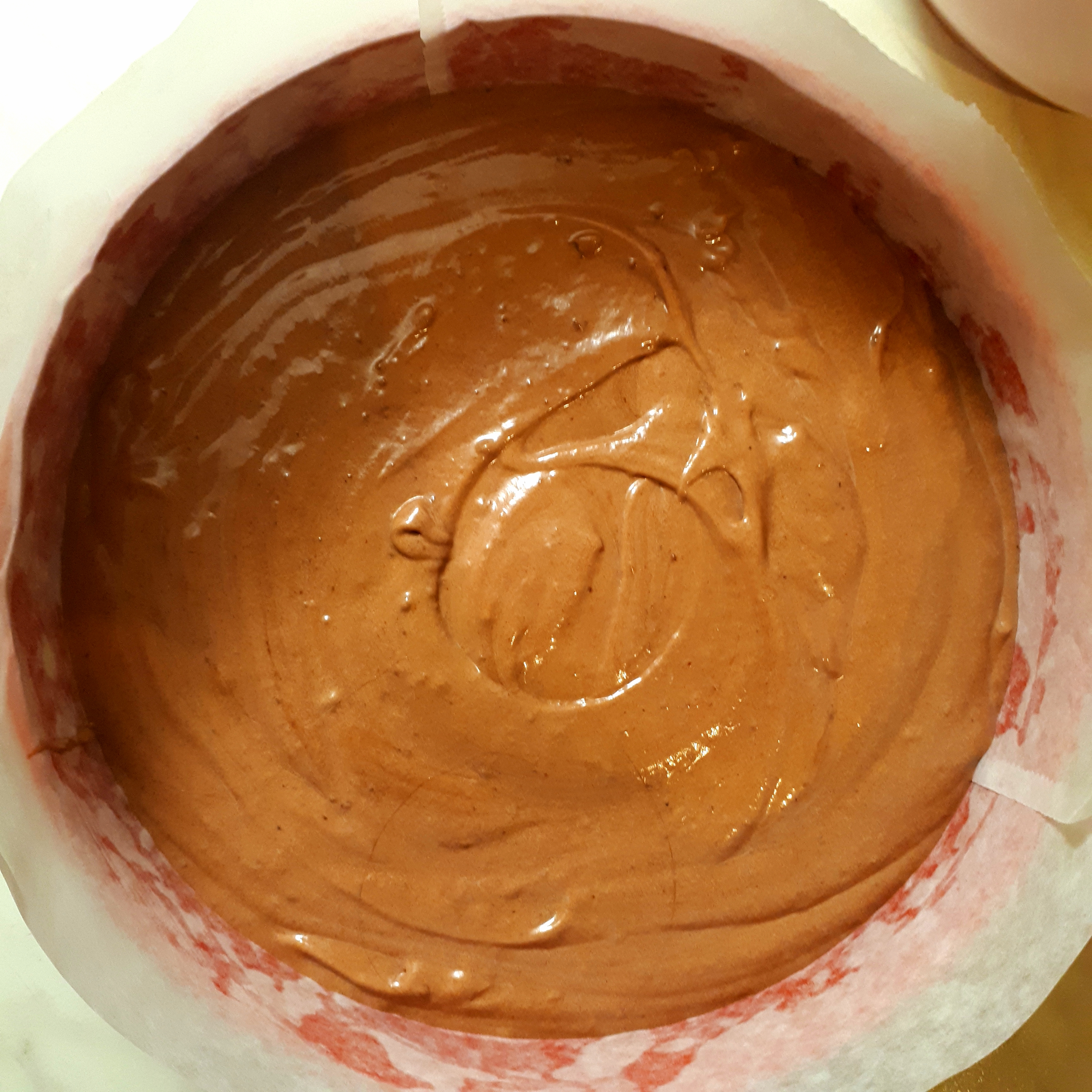 Červená tortová forma vystlaná papierom na pečenie s kakaovým cestom pred pečením