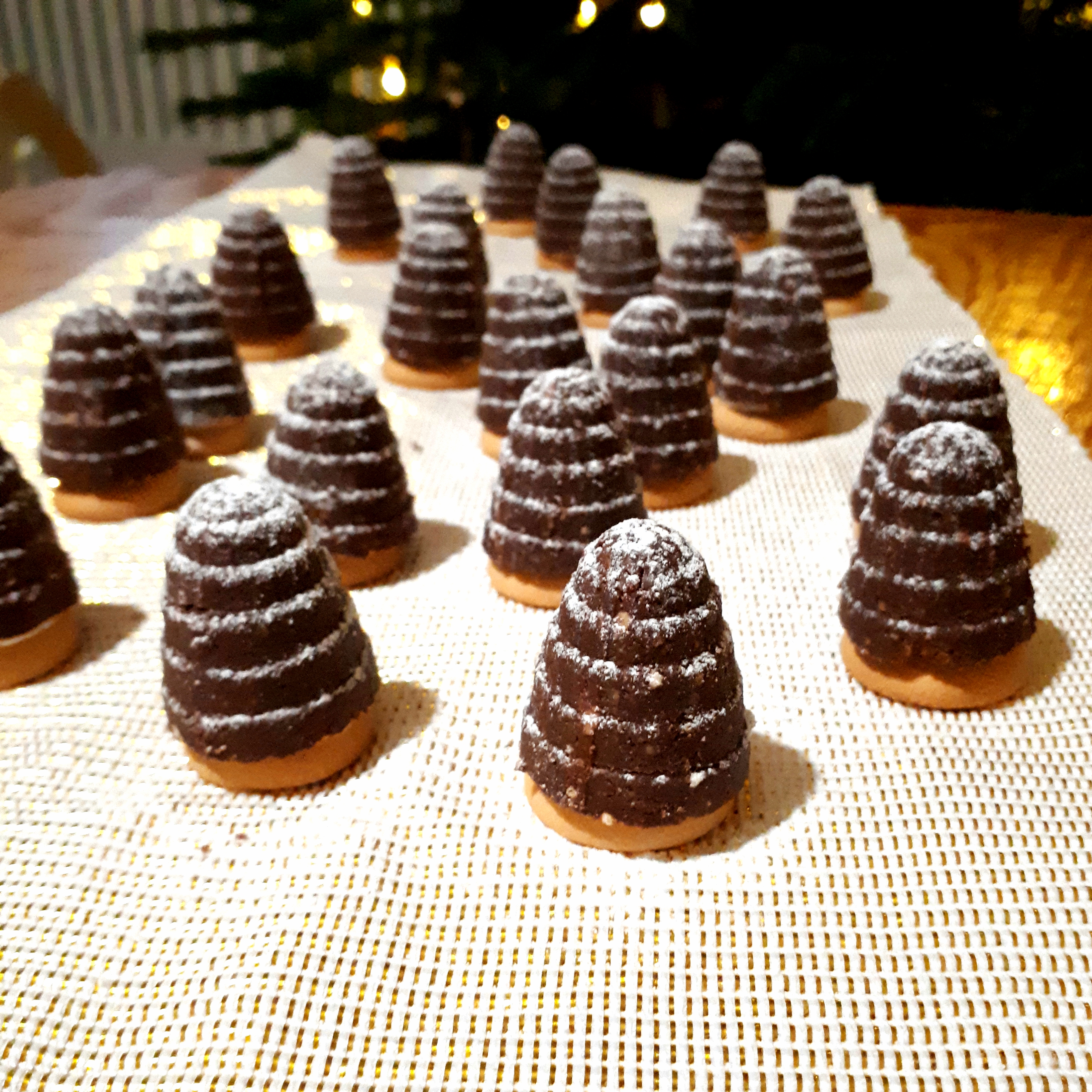 Hotové úliky z kakaového cesta na piškóte posypané práčkovým cukrom na zlatom obruse na drevenom stole v pozadí vianočný stromček