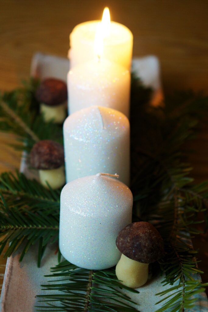 Štyri adventné sviečky na bielej obdĺžnikovejtácke vetvičy ihličia marcipánové hríbiky dve sviečky horia