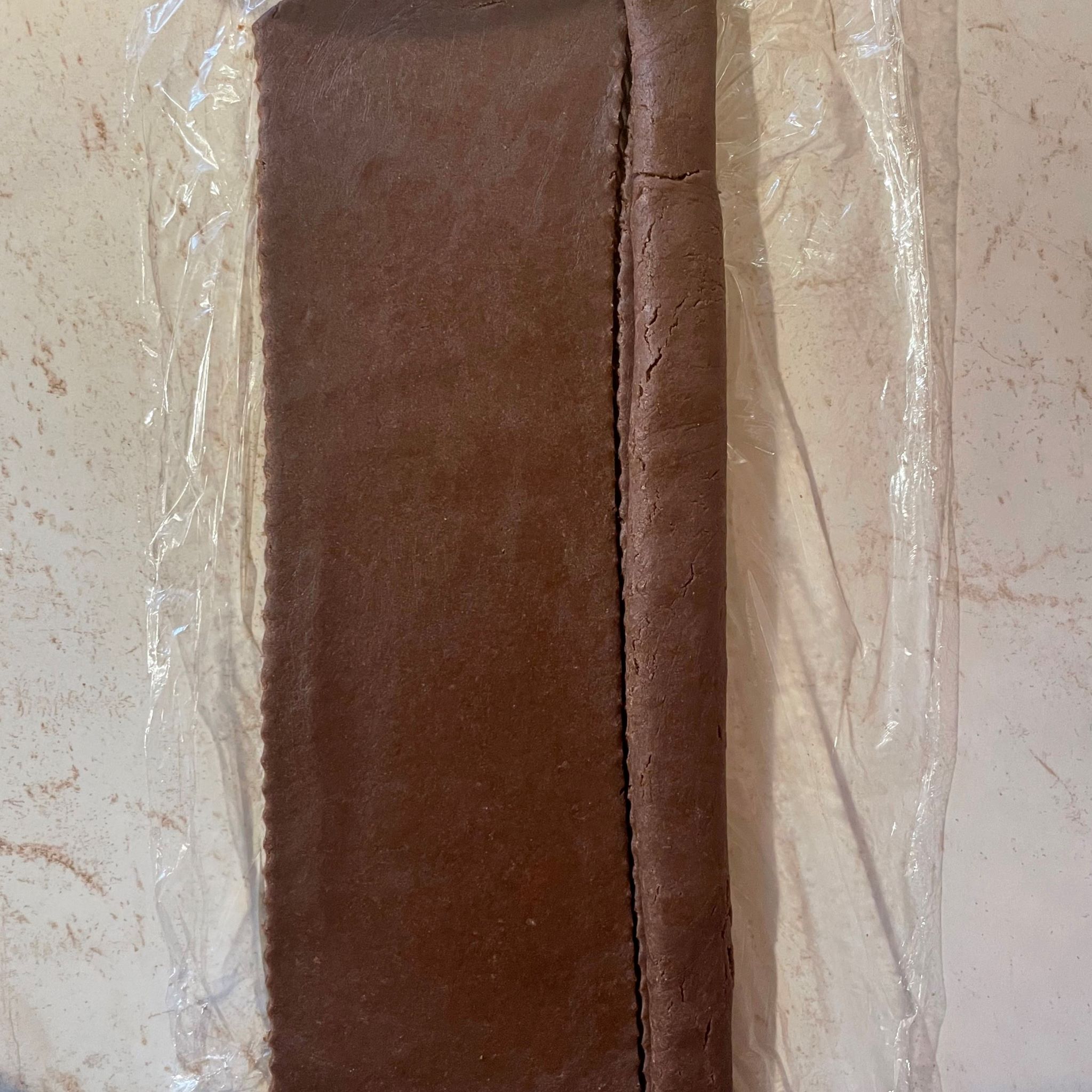 Obdĺžnik rozvaľkaného kakaového cesta na okraji náplň zo slivkového lekváru a perníku zatočená do cesta mramorové pozadie